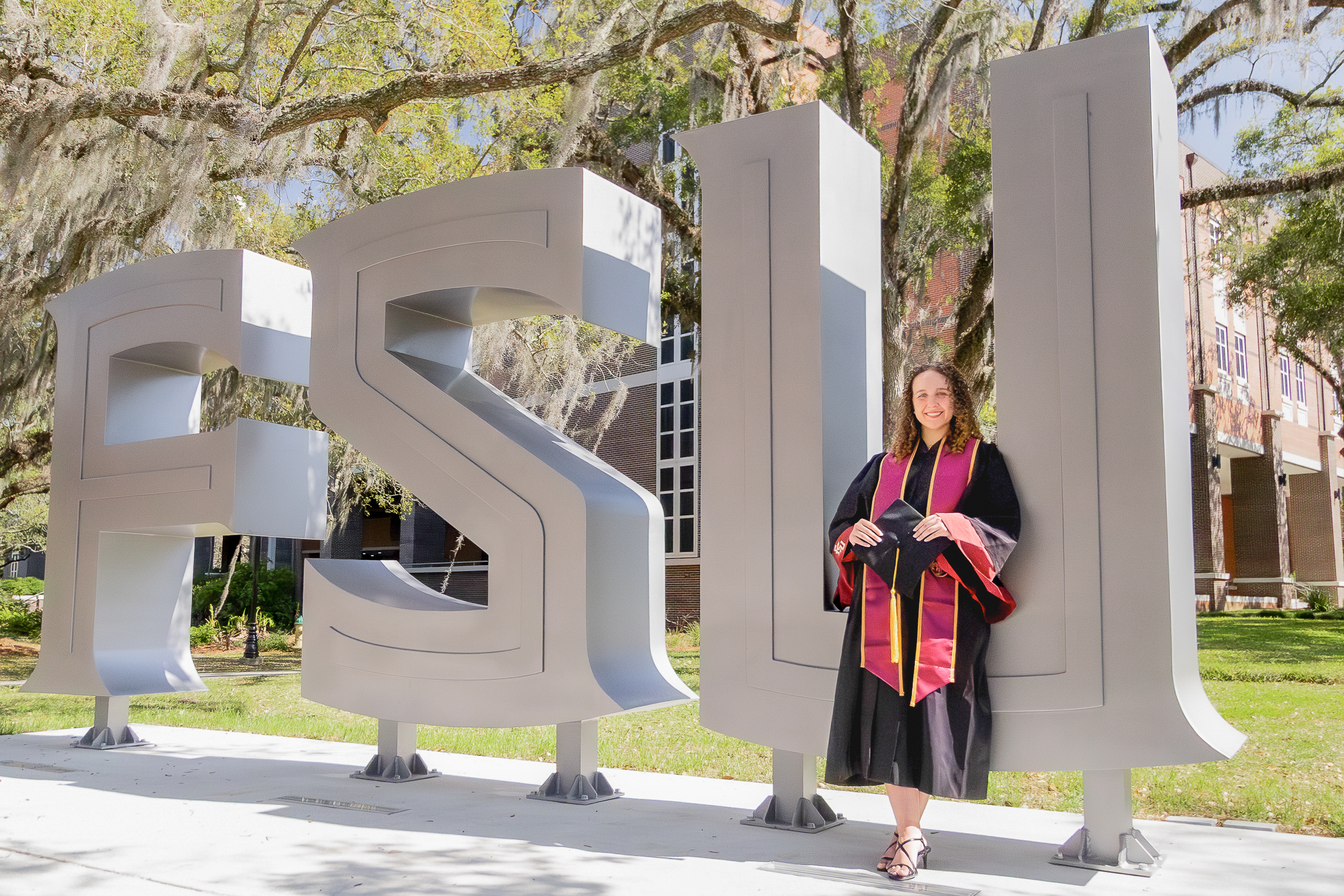 Graduate leaning against large metal FSU letters